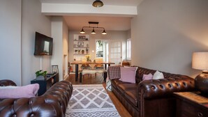 A living room with a brown leather sofa, a patterned rug, and a television mounted on the wall. - HEREFORD CITY – St Owens Terrace: Spacious 3-Storey Home, Walk to Centre (Hereford)