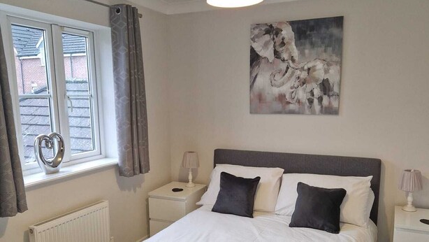 A neatly arranged bedroom with a bed, two bedside tables, a window with curtains, a radiator, and a ceiling light fixture. - HEREFORD – Finch House: Modern 4-Bed, Dog Friendly, Sleeps 10 + Pool Table (Hereford)