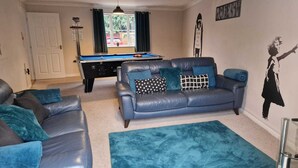 A living room with a pool table, a blue leather sofa, and a blue rug. - HEREFORD – Finch House: Modern 4-Bed, Dog Friendly, Sleeps 10 + Pool Table (Hereford)