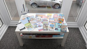 Une table sur laquelle sont disposées diverses brochures et des livres sur le thème du voyage, un stylo et un petit modèle de voilier.