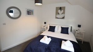 Une chambre à coucher avec un lit, deux tables de chevet, un miroir rond, un tableau encadré et un luminaire au plafond.