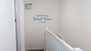 A hallway with a white wall featuring a welcome sign for Strand House in Exmouth. - EXMOUTH, DEVON - Apt 2, Strand House: 2 Bed, Central Location, Sleeps 6, (Exmouth)