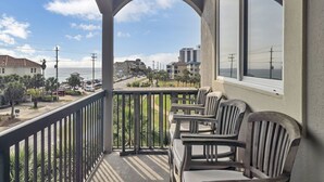 Een balkon met uitzicht op een kustweg, palmbomen en gebouwen op de achtergrond.