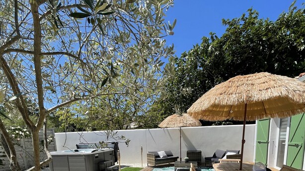 Une terrasse en bois avec des meubles d’extérieur, un parasol en chaume et un espace piscine.
