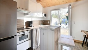 Une cuisine moderne équipée d’un réfrigérateur en acier inoxydable, de meubles blancs, d’un four à micro-ondes et d’une machine à café. Le plafond est en bois et une porte-fenêtre coulissante donne accès à un espace extérieur.