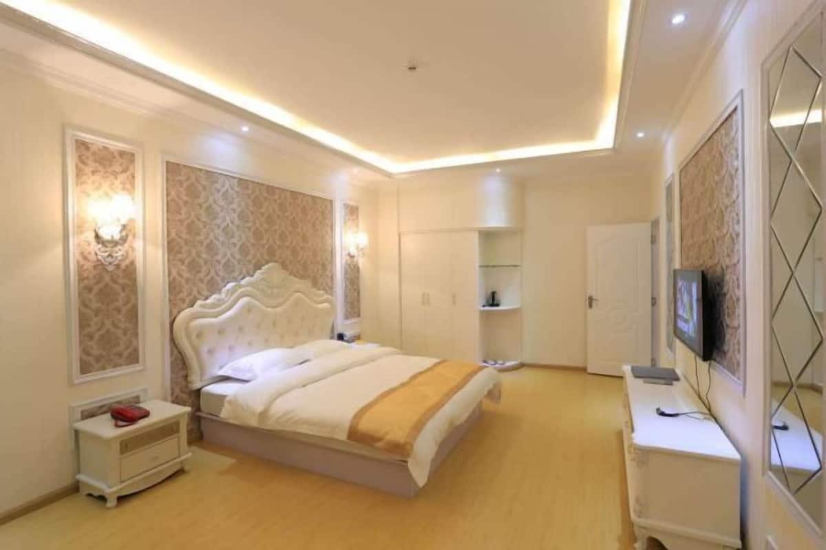 A bedroom with a large bed, bedside tables, a wardrobe, a TV, and a desk.