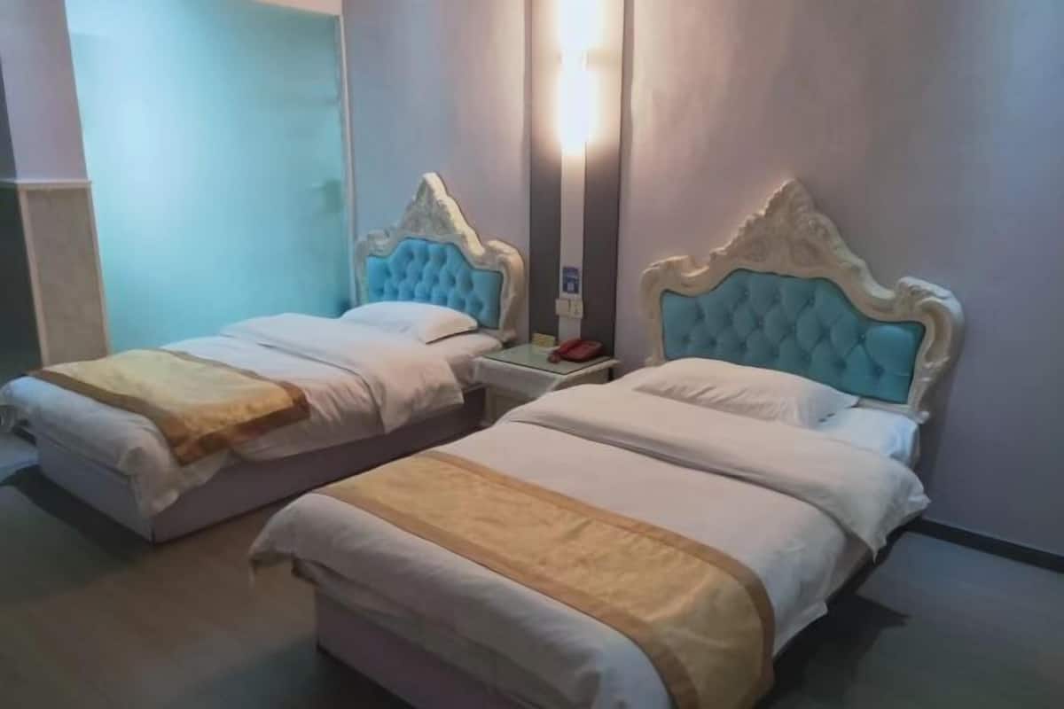 Two twin beds with matching headboards and footboards, a bedside table with a lamp, and a wall-mounted light fixture.