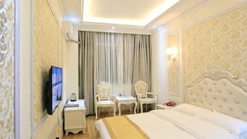 A hotel room with a bed, two chairs, a TV, a desk, and a window with curtains.