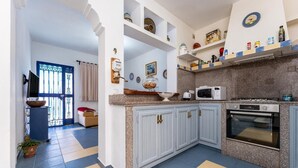 Une cuisine avec des meubles blancs, un four à micro-ondes, un four traditionnel et une machine à café. Une fenêtre offre une vue sur l’extérieur.