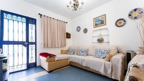 Un salon avec un canapé, une couverture rouge, un lustre et une porte dotée d’un cadre bleu.