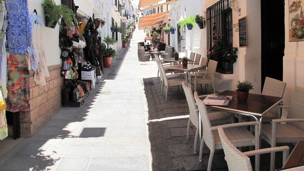 Une rue étroite bordée de boutiques et dotée de terrasses.