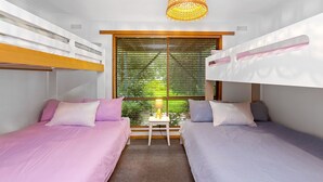 A room with bunk beds, a small table with a lamp, and a window with blinds.