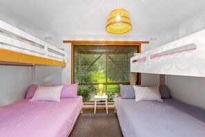 A room with bunk beds, a small table with a lamp, and a window with blinds.