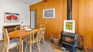 A wooden-paneled room with a dining table, chairs, a framed picture, and a wood-burning stove. - Frankie - A wonderful place to escape the city (Skenes Creek)