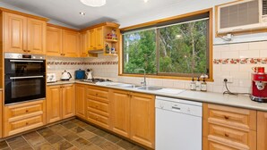 A kitchen with wooden cabinets, a built-in oven, a dishwasher, and a window with a view of greenery.