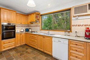 A kitchen with wooden cabinets, a built-in oven, a dishwasher, and a window with a view of greenery.