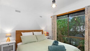 A neatly made bed with pillows, a bedside lamp, and a window with curtains. - Frankie - A wonderful place to escape the city (Skenes Creek)