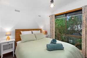 A neatly made bed with pillows, a bedside lamp, and a window with curtains. - Frankie - A wonderful place to escape the city (Skenes Creek)