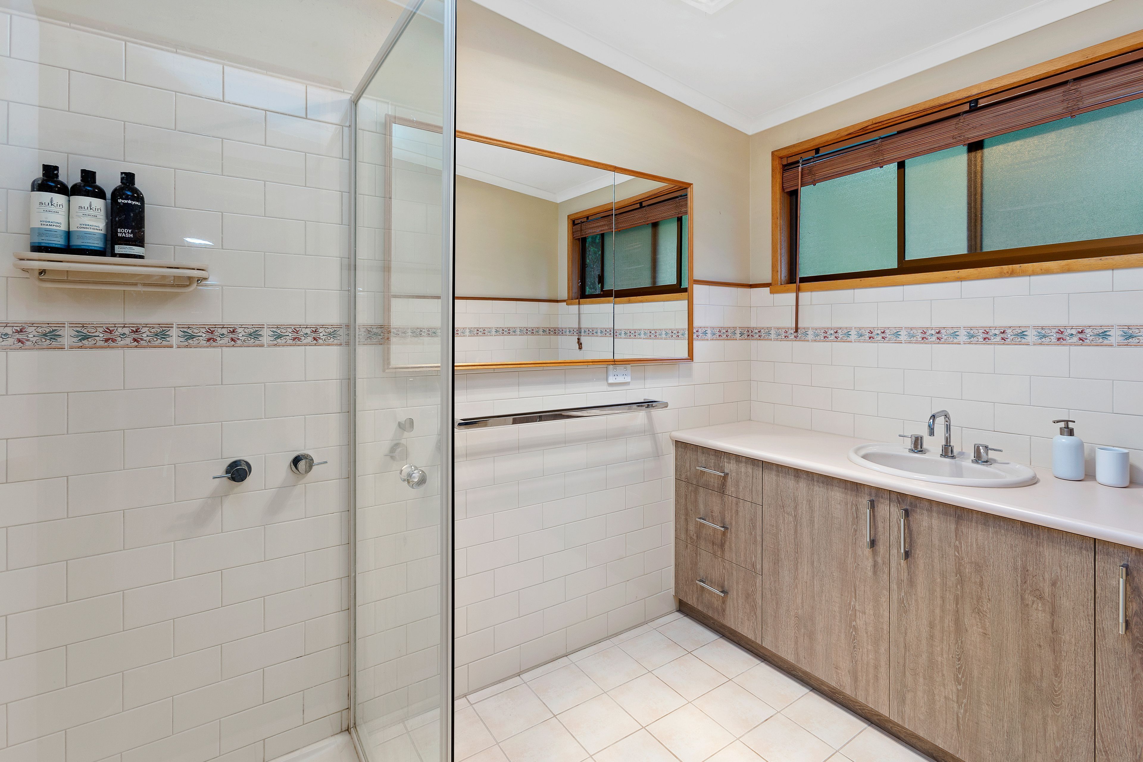 Un baño moderno con cabina de ducha de vidrio, tocador de madera con lavamanos y espejo sobre el tocador.