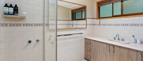 Un baño moderno con cabina de ducha de vidrio, tocador de madera con lavamanos y espejo sobre el tocador.
