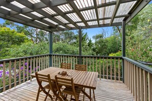 A wooden deck with a table and chairs, surrounded by a metal railing and lush greenery.