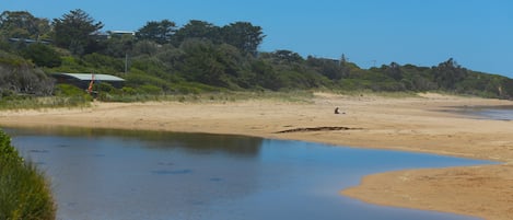 A beach with a calm water body, sandy shore, and a building with a green roof in the background.