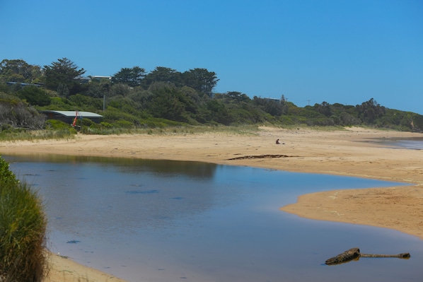 A beach with a calm water body, sandy shore, and a building with a green roof in the background.