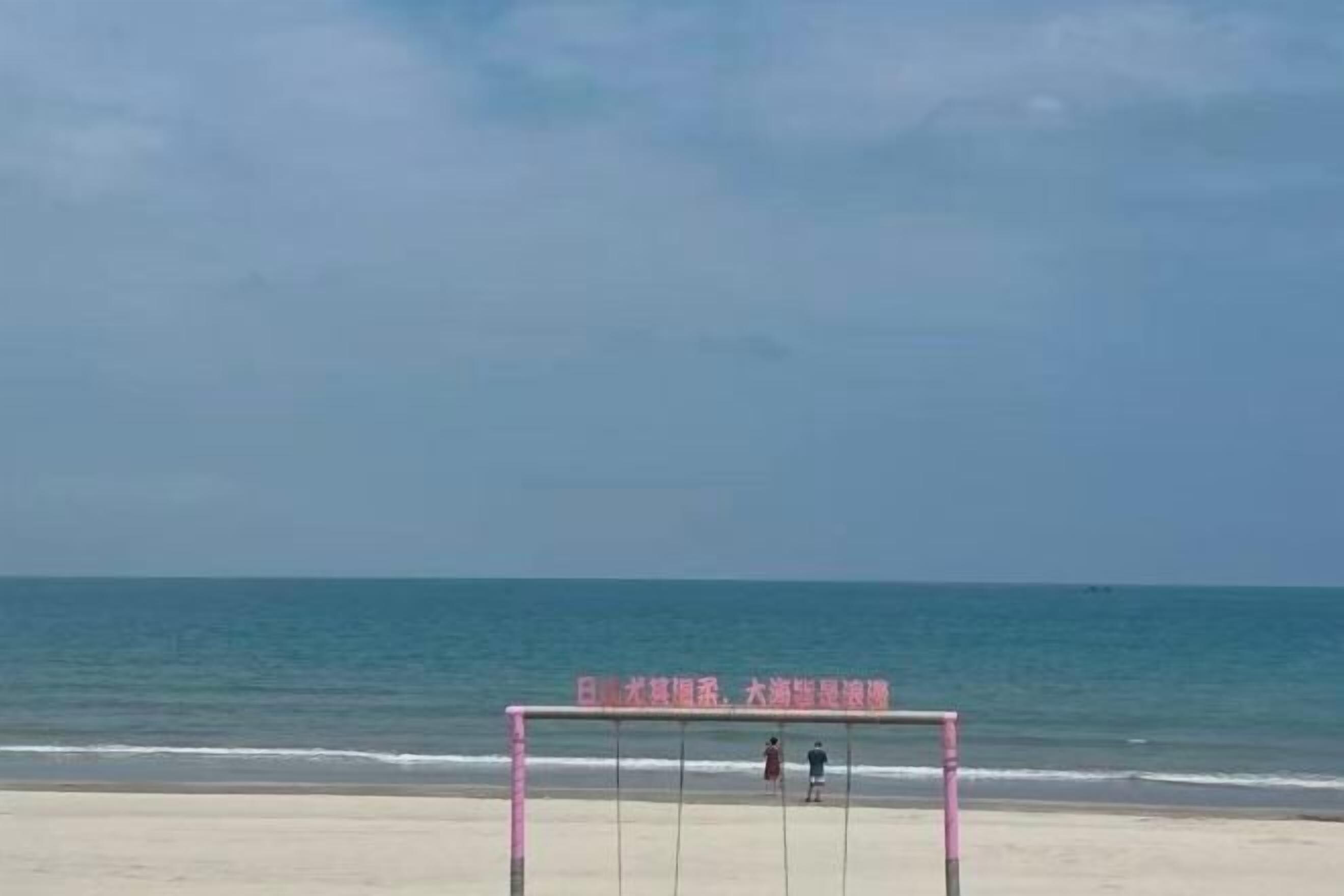A beach volleyball net with two people standing on it, overlooking the ocean.