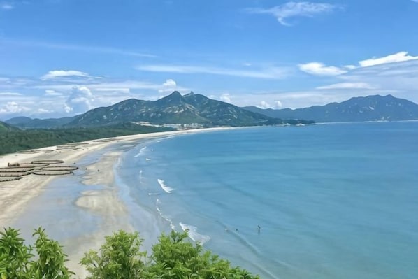 A beach with clear water, a sandy shore, and mountains in the background.
