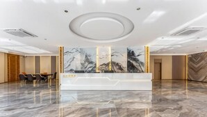 Uma área de recepção de hotel com piso de mármore, balcão de atendimento e um grande mural na parede.