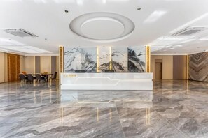 Zona de recepción de hotel con piso de mármol, mostrador y un mural grande en la pared.