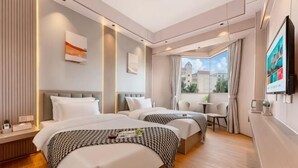 Quarto de hotel com duas camas, uma mesinha, uma televisão e janela com vista para prédios.