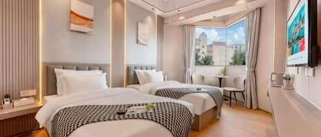 A hotel room with two beds, a small table, a TV, and a window with a view of buildings.