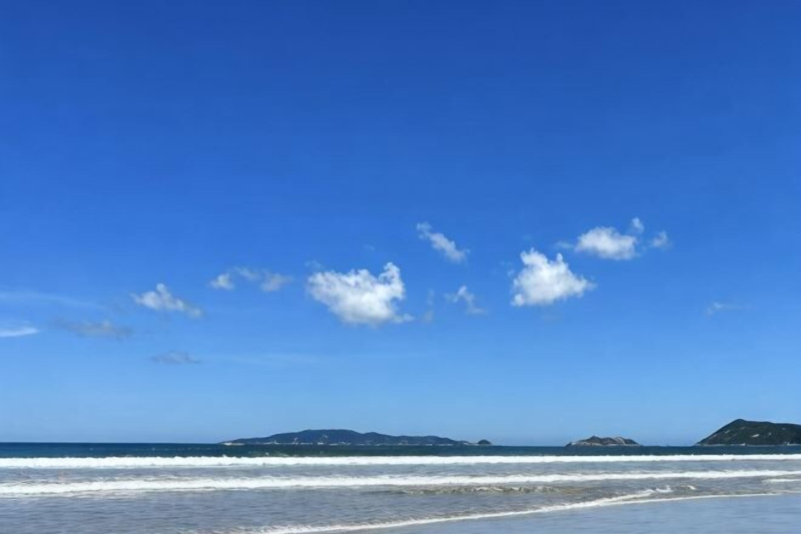 Una playa con cielo despejado, olas y islas a lo lejos.