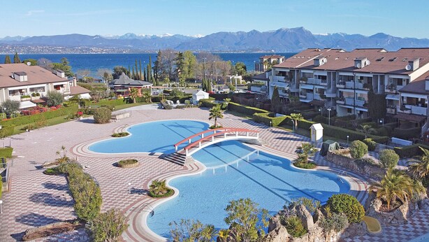 A resort with a large pool, a bridge, and mountain views. - Lauri 0/18 by Wonderful Italy (Desenzano del Garda)