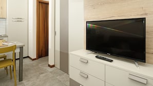 A modern kitchen with a built-in TV, wooden cabinets, and a dining area with a yellow chair. - Lauri 0/18 by Wonderful Italy (Desenzano del Garda)