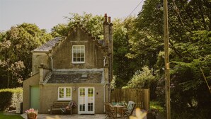 A quaint stone house with a green door, a small porch with a bench, and a wooden fence.