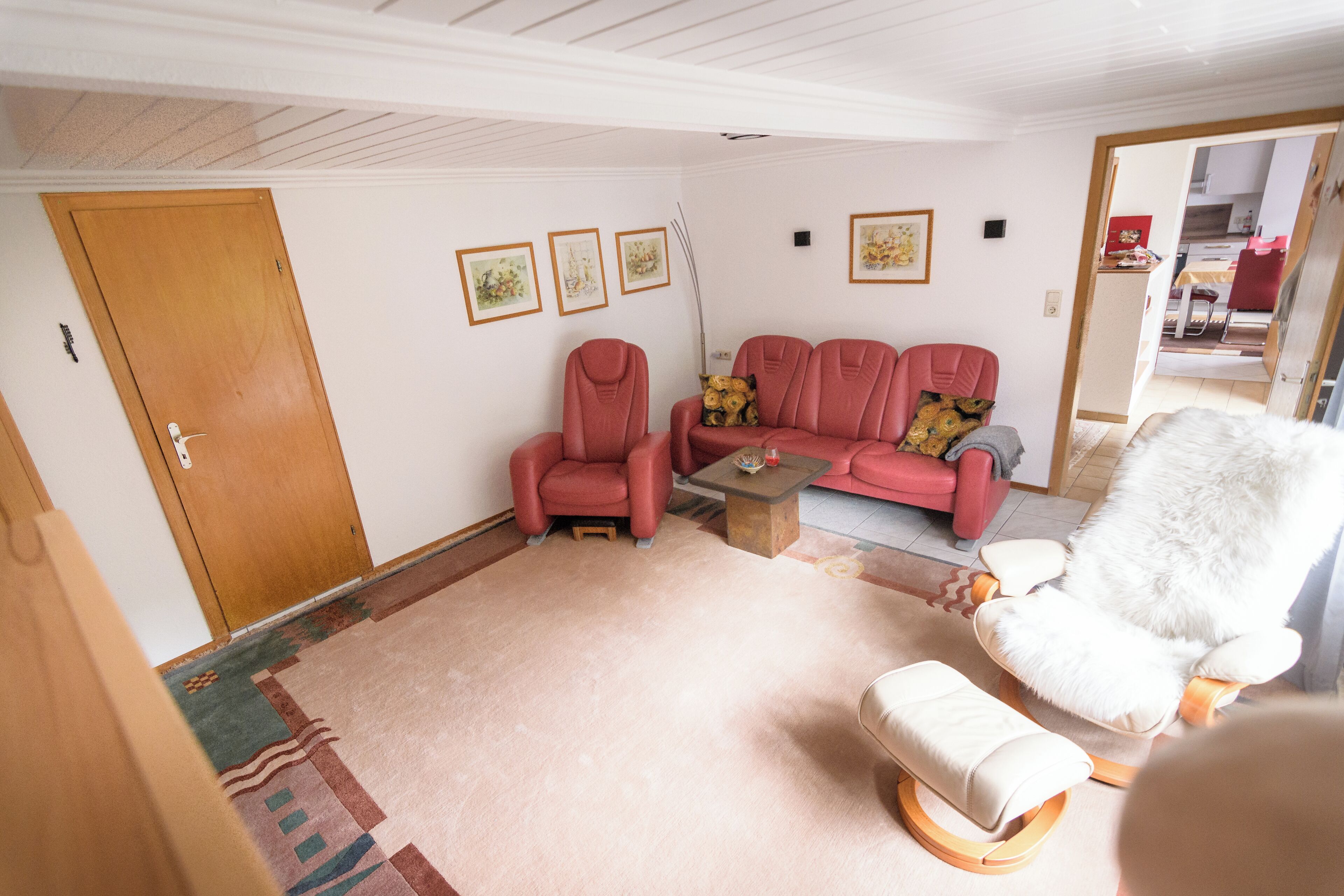A living room with a wooden door, a red sofa, a white armchair, and a small table.