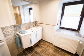 A bathroom with a white vanity, a mirror, a window with a view, and patterned tiles on the wall.