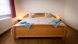 Una cama con estructura de madera, dos mesitas de noche, un radiador blanco y una ventana con cortinas.