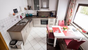 Cocina compacta con armarios blancos, horno integrado y comedor con mesa y sillas rojas.