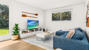 Un salon moderne avec un téléviseur à écran plat, des décorations en forme de planches de surf en bois, une grande plante en pot et un canapé bleu.