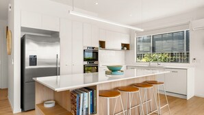 Une cuisine moderne dotée d’un grand îlot central, d’un four encastré et d’une fenêtre donnant sur un paysage verdoyant.