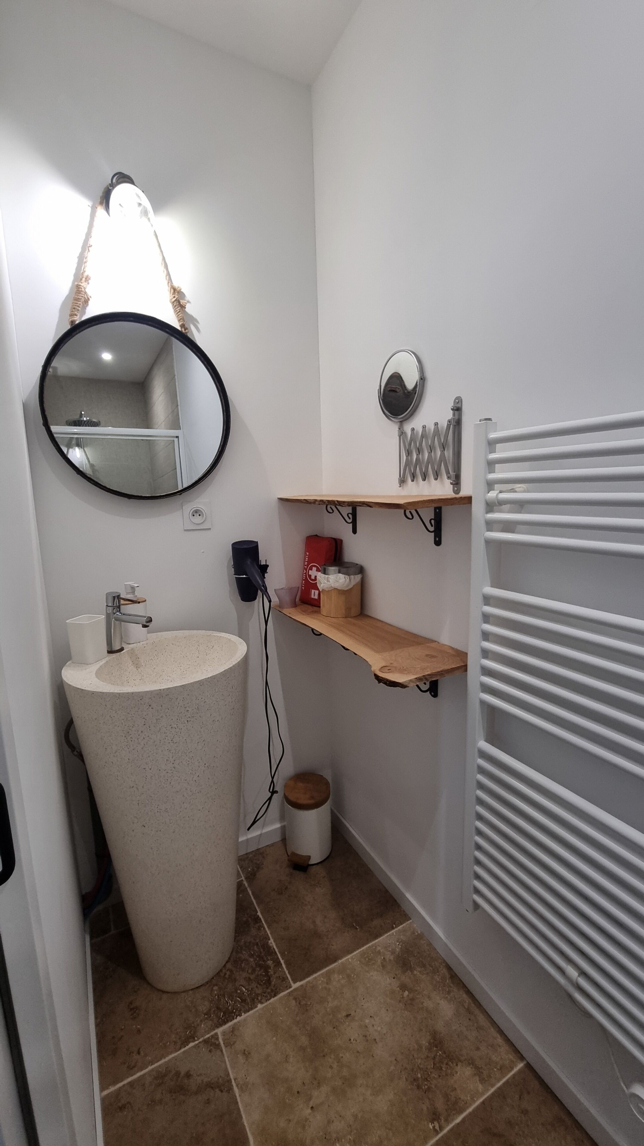 A bathroom with a freestanding sink, a round mirror, a towel rack, a shelf with toiletries, and a radiator.