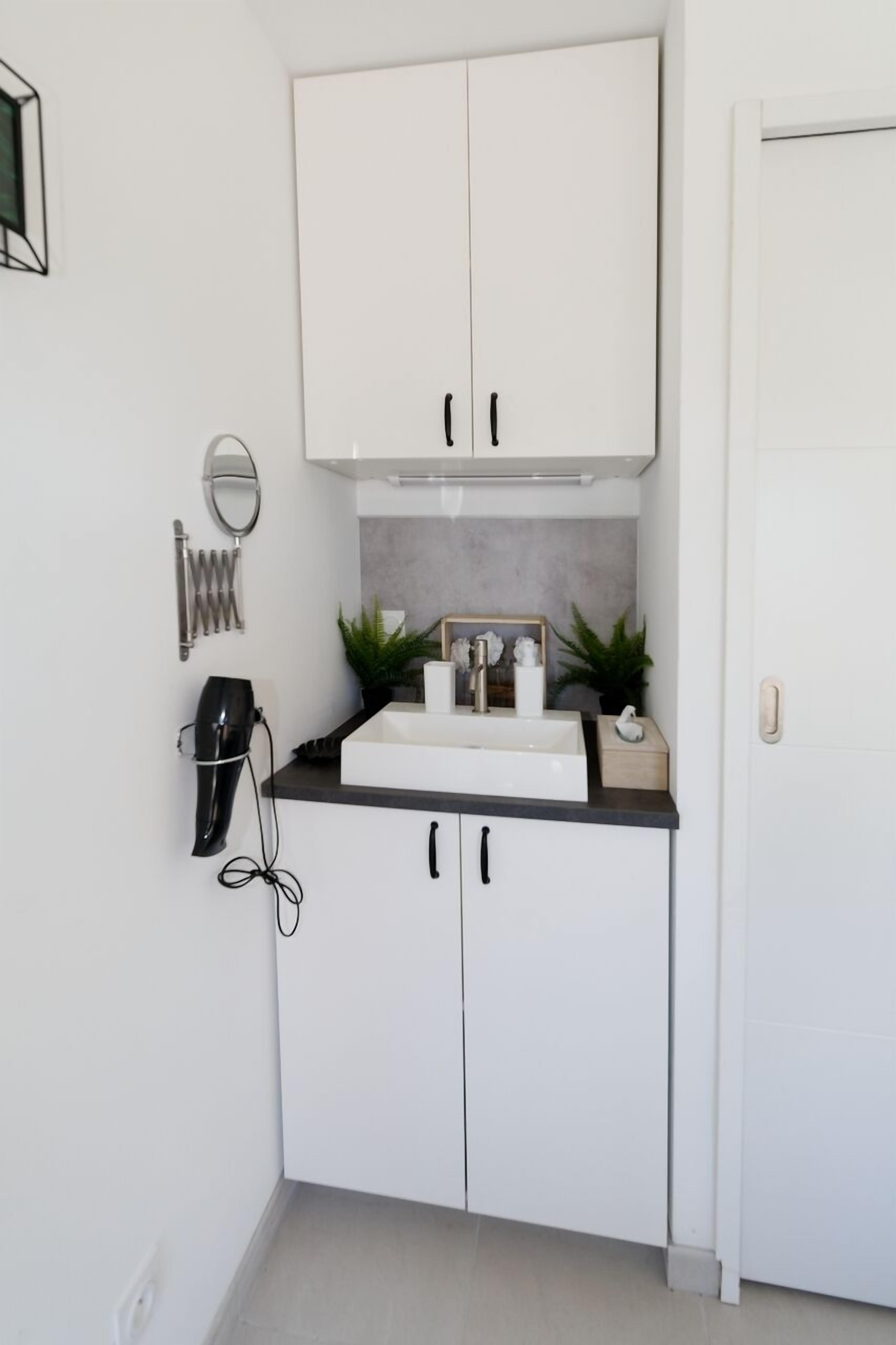 Una cocina compacta con armarios blancos, un lavamanos en la encimera y un espejo.