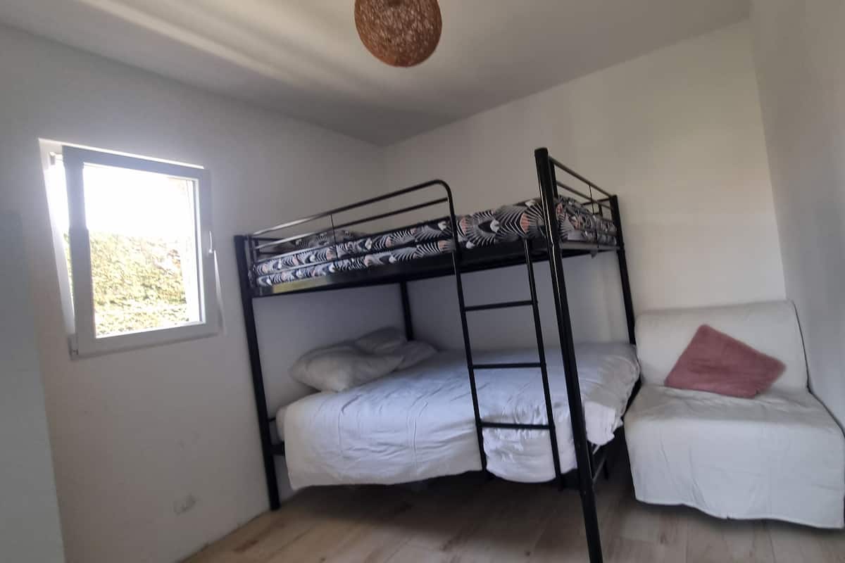 A bunk bed room with a window, a wooden floor, and a hanging light fixture.