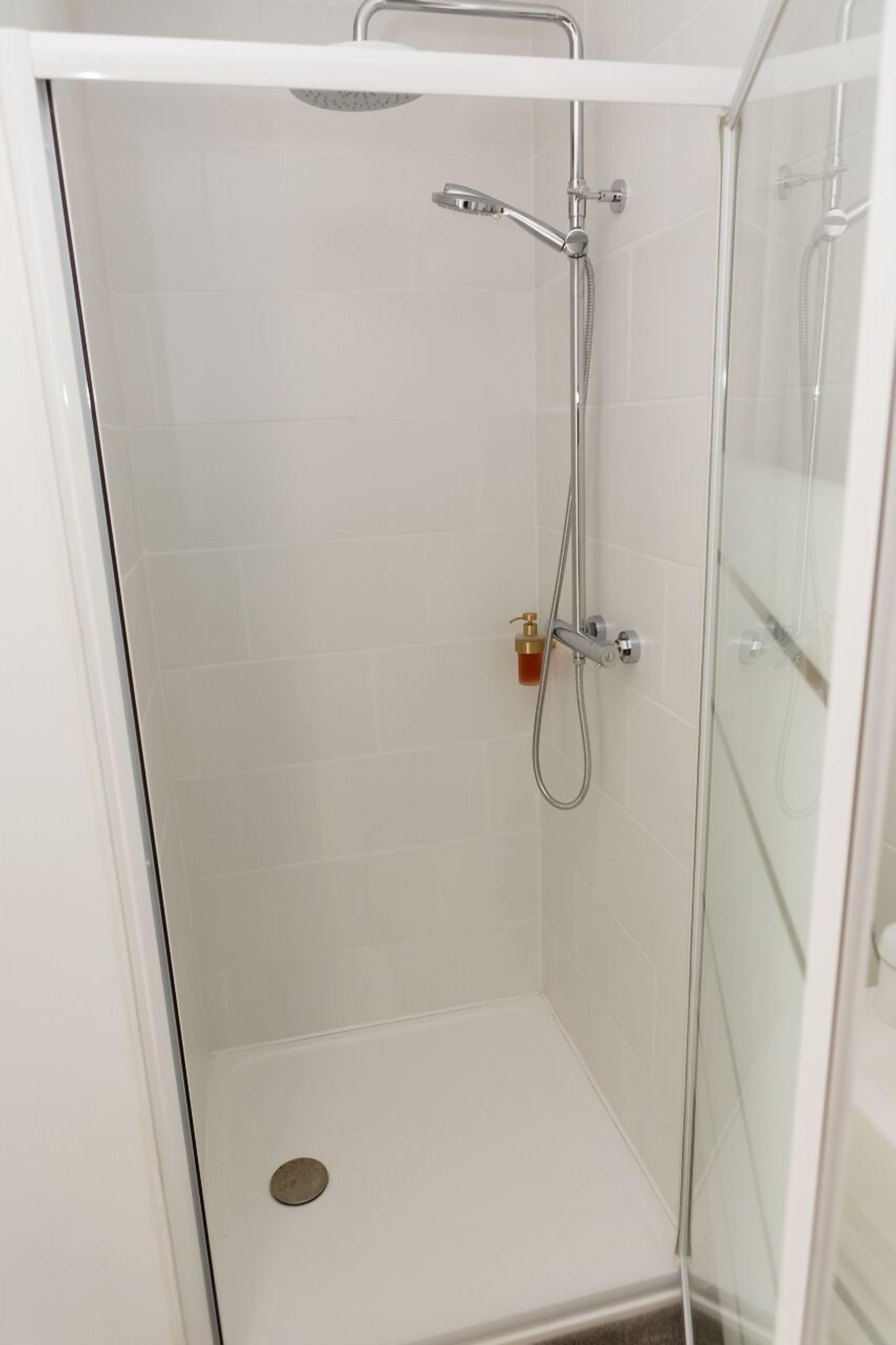 A glass-enclosed shower stall with a handheld showerhead and a wall-mounted faucet.