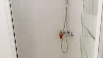 A glass-enclosed shower stall with a handheld showerhead and a wall-mounted faucet.