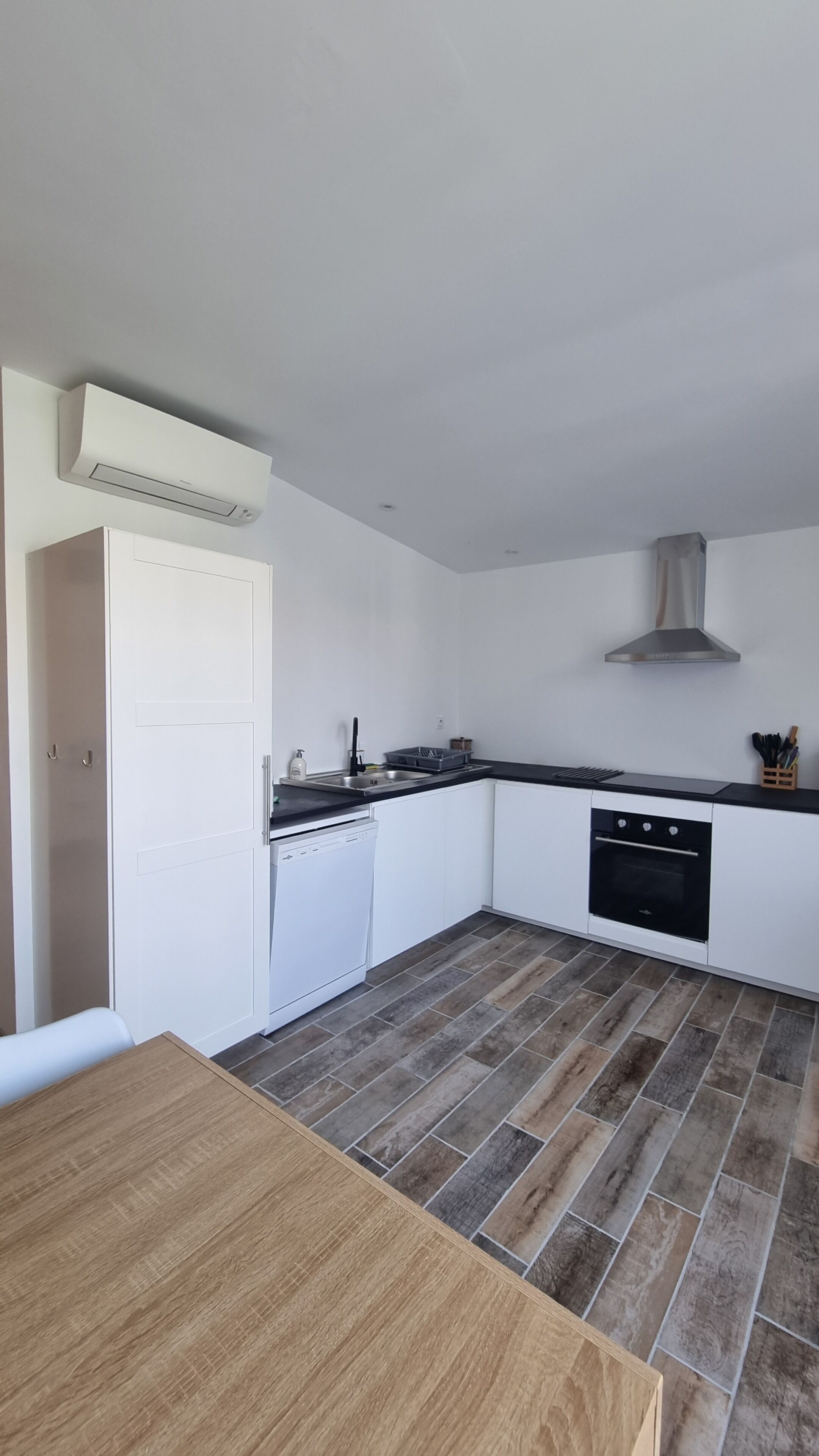 Eine moderne Küche mit weißen Schränken, einer schwarzen Arbeitsplatte, einem eingebauten Backofen und einer Edelstahl-Dunstabzugshaube.