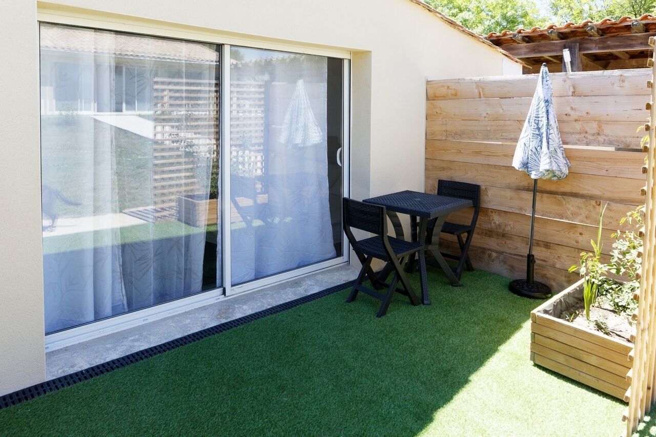A patio with a sliding glass door, a small table, two chairs, and a wooden planter with a plant.